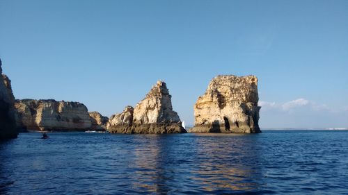 Rock formations in sea against clear blue sky