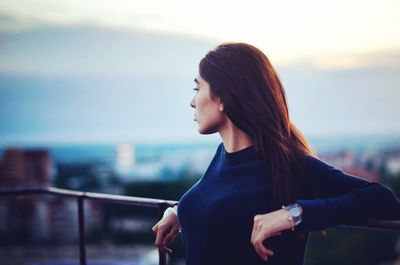 Side view of a young woman holding railing against sea