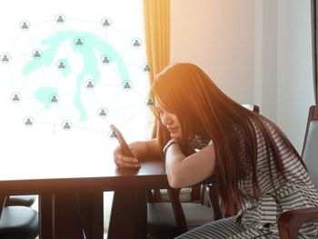 Side view of woman using phone while sitting on table