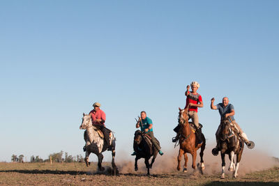 Group of people riding on field against clear sky