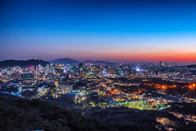 Aerial view of illuminated cityscape against blue sky during sunset