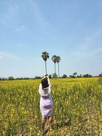 Rear view of woman with yellow flowers on field