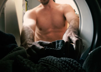 Midsection of man putting clothes in washing machine