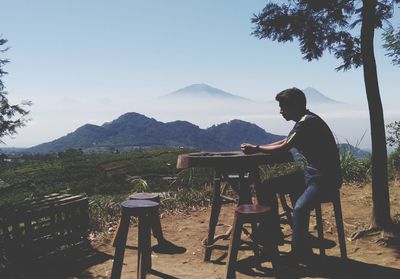 Man sitting on seat at mountain against sky