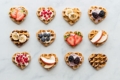 Mini heart shaped waffles with various toppings, against a light background.