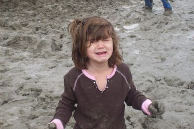 Little girl with dirty hand crying at muddy beach