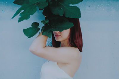 Side view of woman holding plants against wall