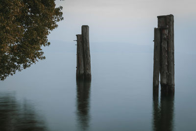 Calm day on the lake. wooden post in lake against sky
