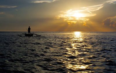 Silhouette man in sea against sky during sunset