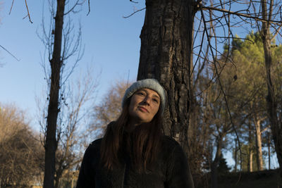 Portrait of young woman standing by tree against sky