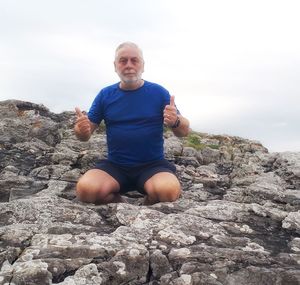 Portrait of man smiling on rock against sky