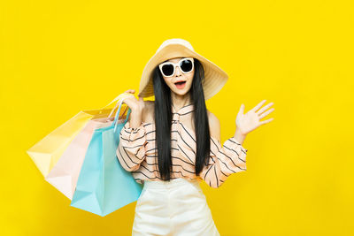 Portrait of young woman wearing sunglasses against yellow background