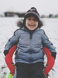 Portrait of laughing boy sitting on chair during winter