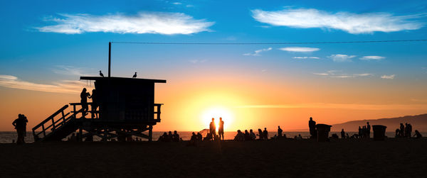 Silhouette people on beach against sky during sunset