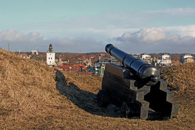 Cannon to buildings on field against sky