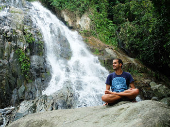 Young man sitting by waterfall