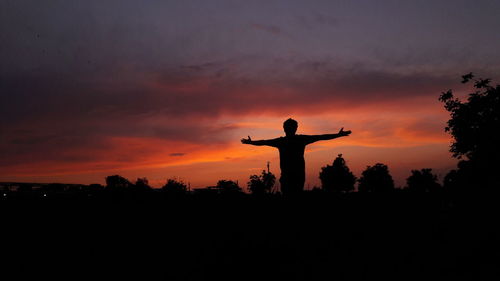 Silhouette man with arms raised standing against sky during sunset