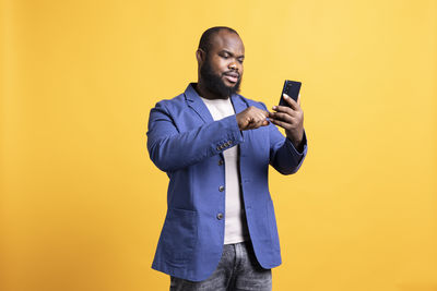 Young man using mobile phone while standing against yellow background