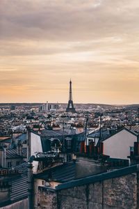 Mid distance view of eiffel tower amidst buildings against cloudy sky at sunset