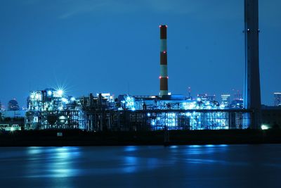 Illuminated factory against clear blue sky at night