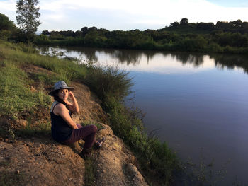 Woman sitting on rock by lake against sky