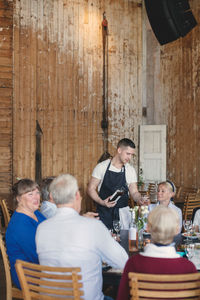 Young waiter serving wine to senior friends at table in restaurant
