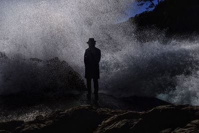 Silhouette man standing on rock at sea