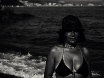 Portrait of woman in bikini standing at beach against sky