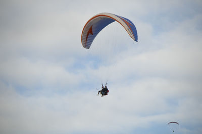 Low angle view of people paragliding against sky