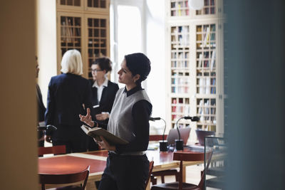 Female lawyer gesturing while coworkers standing in background at library