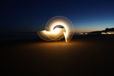 Man standing by illuminated lighting equipment at beach against sky at night