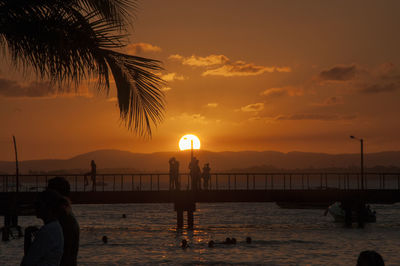 Silhouette people on beach against sky during sunset