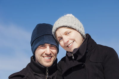 Portrait of smiling couple standing against blue sky during winter
