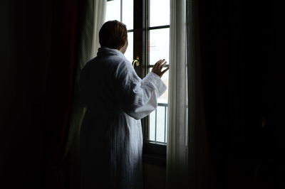 Rear view of woman looking through window at home