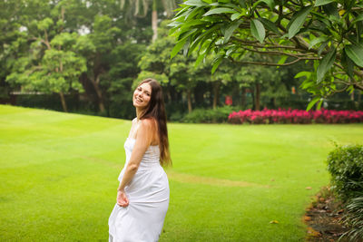 Portrait of smiling young woman standing against green plants