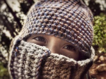 Close-up of person covering face with knitted warm clothing while looking away