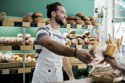 Smiling male owner giving bread to customer in bakery