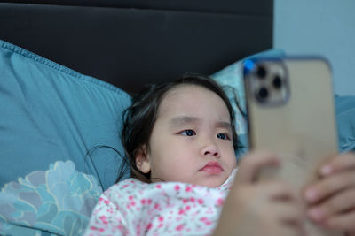 Close-up of girl using phone while lying on bed at home