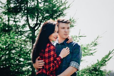 Young couple looking away while standing in forest during sunny day