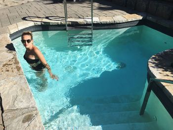 High angle portrait of young woman wearing sunglasses standing in pool