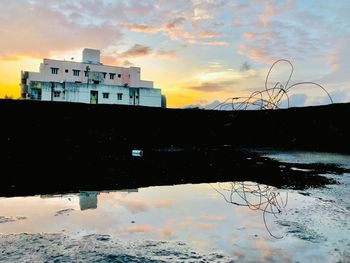 Reflection of buildings on lake against sky during sunset