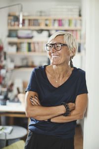 Happy product designer looking away while standing arms crossed at home