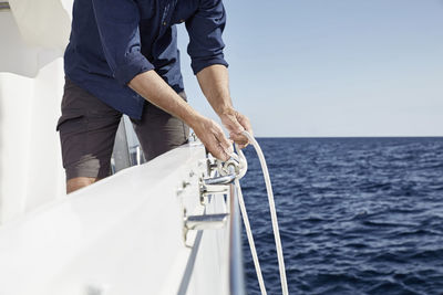 Man on motor yacht tying a knot, partial view