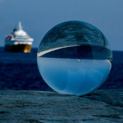 Close-up of crystal ball on beach against clear blue sky