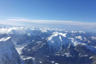 Aerial view of snowcapped mountains against blue sky