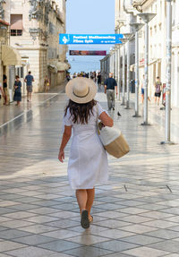 Young woman wearing sundress and hat, walking down marmont street in split, croatia