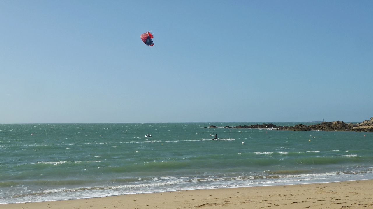 sea, water, sky, beach, horizon over water, land, horizon, sport, beauty in nature, scenics - nature, adventure, clear sky, nature, extreme sports, day, motion, wave, copy space, blue, outdoors, kiteboarding, parasailing