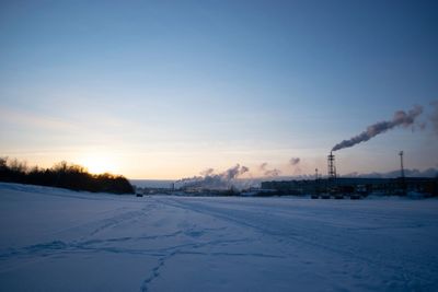 Snow covered field against sky during sunset