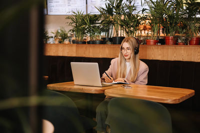 A smiling student wearing glasses and headphones works and studies online using wireless technology