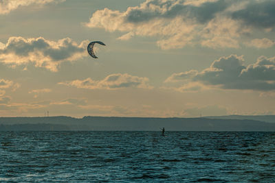 Silhouette person paragliding over sea against sky